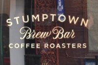 The writing on the window of the Brew Bar part of Stumptown, W 8th St,, New York City. "STUMPTOWN" over "COFFEE ROASTERS" in capitals, with "Brew Bar" in cursive script in between.