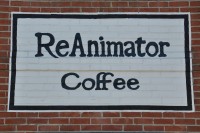 ReAnimator Coffee, painted black on a white background on the brick wall above the door.