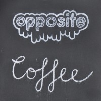 The Opposite logo in white chalk on a black background, with the word 'Coffee' written underneath.