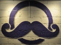 The Siempre Bicycle Café logo, a stylised face with a handlebar moustache, painted in black on the white brick wall at the café .