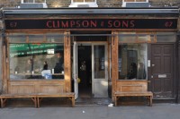 The front of the Climpson and Sons Café, with the recessed door offset to the right and with wooden benches on the pavement in front of the windows.
