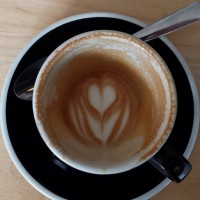Shot of a tulip cup on a black saucer, taken from above. The coffee is almost gone, but the latte art pattern, a tulip, is still plainly visible in the remainder of the milk in the bottom of the cup.