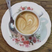 A lovely, creamy piccolo in a classic espresso cup, seen from above on an over-sized floral saucer.