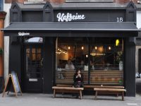 The front of Kaffeine, door to the left, windows to the right, with a pair of benches in front of the window acting as tables.