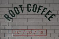 The words "Root Coffee" written in an arch in black capitals on white, tiled wall. "EST / 20 / 15" is written in red in a box below.