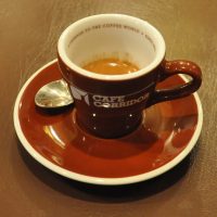 A single-origin Colombian espresso in a branded cup from Cafe Corridor in Hong Kong with 'A passage to the coffee world since 2001' written on the inside rim.