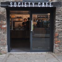 The main entrance to Society Cafe in Bristol, a pair of glass double-doors opening out onto Farr's Lane, with the counter directly ahead.