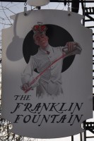 The Franklin Fountain sign, showing a man in a white uniform, mixing sodas.