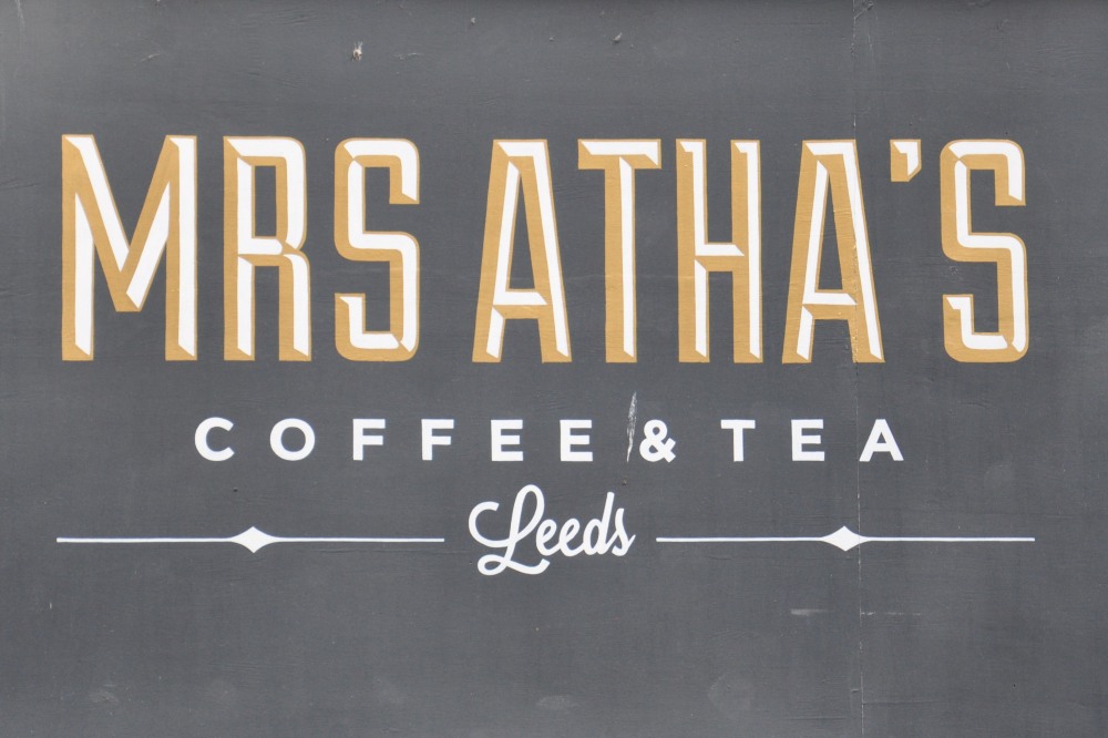 The Mrs Atha's Logo: the words "Mrs Atha's" in gold capitals, with the words "Coffee & Tea" written beneath, all above the word "Leeds" written in script.