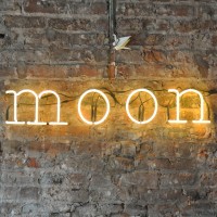 A neon sign, "moon" on the bare brick chimney breast of Moon Beer & Coffee in Chester