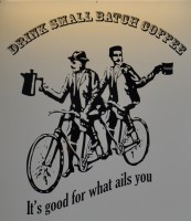 The Small Batch Logo: two gentlemen on a tandem, one holding a coffee pot, the other a mug. Above is written "DRINK SMALL BATCH COFFEE" and below "It's good for what ails you".