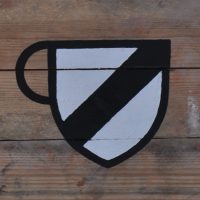An old-fashioned, heraldic shield, in white, with a black diagonal line running through it, bottom left to top right, with a handle added on the left to turn it into a coffee cup