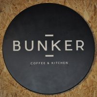 The word BUNKER written in white, in the centre of a large black circle, with the smaller words "COFFEE & KITCHEN" written below/
