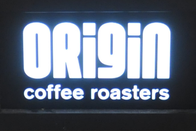 The words "ORigiN coffee roasters" in illuminated white on a black background