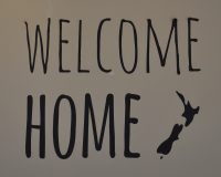 "Welcome Home" says the sign on the wall of Eden Cafe in Witney, next to a stylised map of New Zealand.