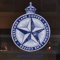 The Bluestone Lane logo (a five-pointed star in a blue circle) from the window of the cafe on Locust Street in Philadelphia.