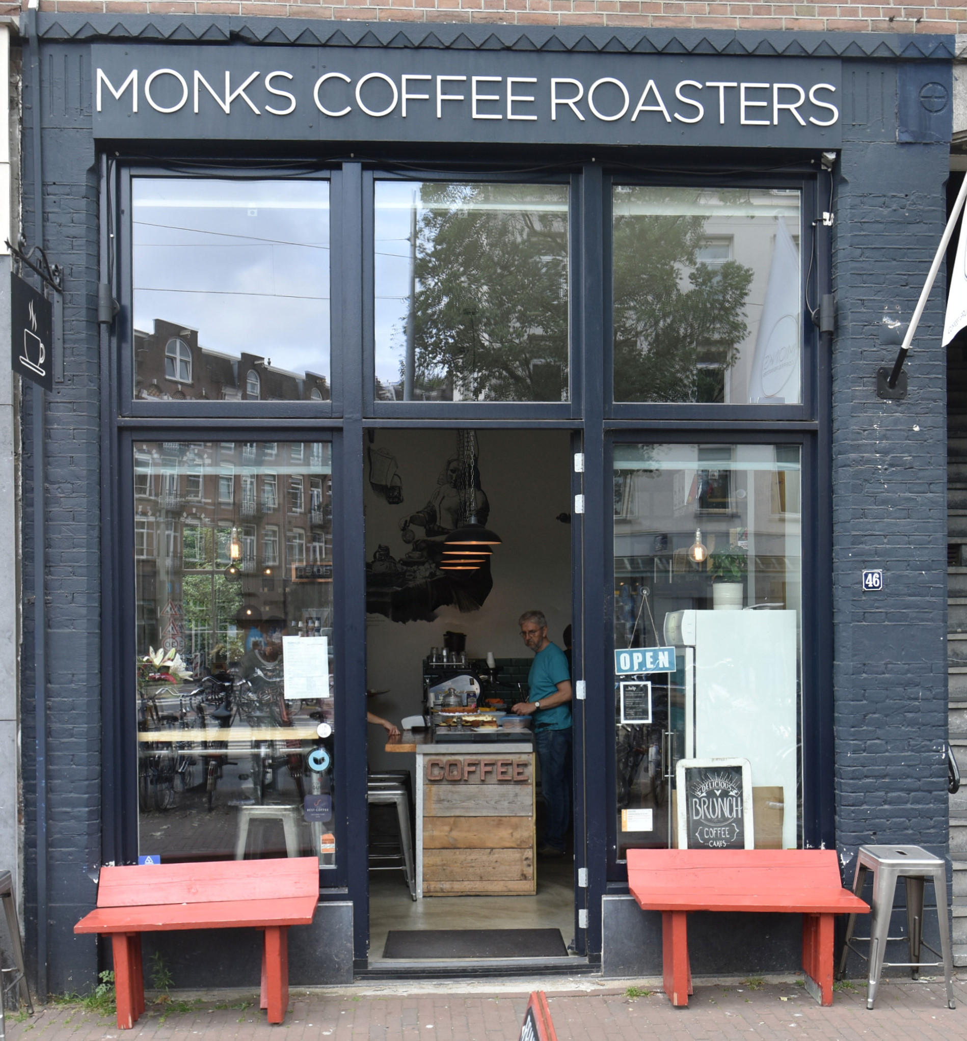 Monks Coffee Roasters on Bilderdijkstraat in Amsterdah, with benches either side of the door and the counter clearly visible.
