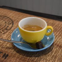 My espresso, a single-origin Honduras from Clifton Coffee Roasters, served in an over-sized yellow up on a blue saucer, with a bite-sized piece of chocolate brownie at Woof Coffee in Teddington.