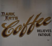 The logo from the back of the wall of I Will Kill Again, proudly proclaiming 'Dark Arts Coffee Relieves Fatigue'.