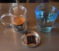 The signature espresso at Le Cafe Alain Ducasse in Coal Drops Yard, Kings Cross, served in a double-walled glass cup and a small square of chocolate.