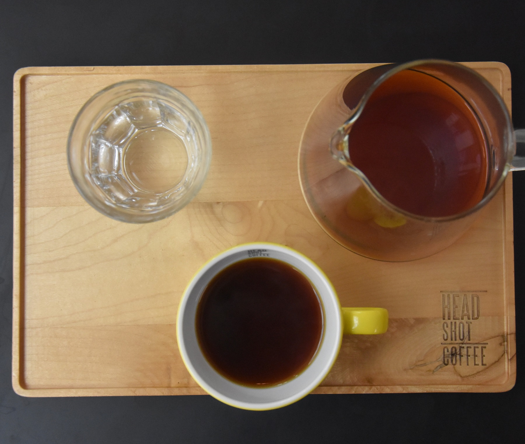 A V60 of a Kenyan single-origin served by Head Shot Coffee in a carafe on a wooden tray, with the cup of the side, along with a glass of water.