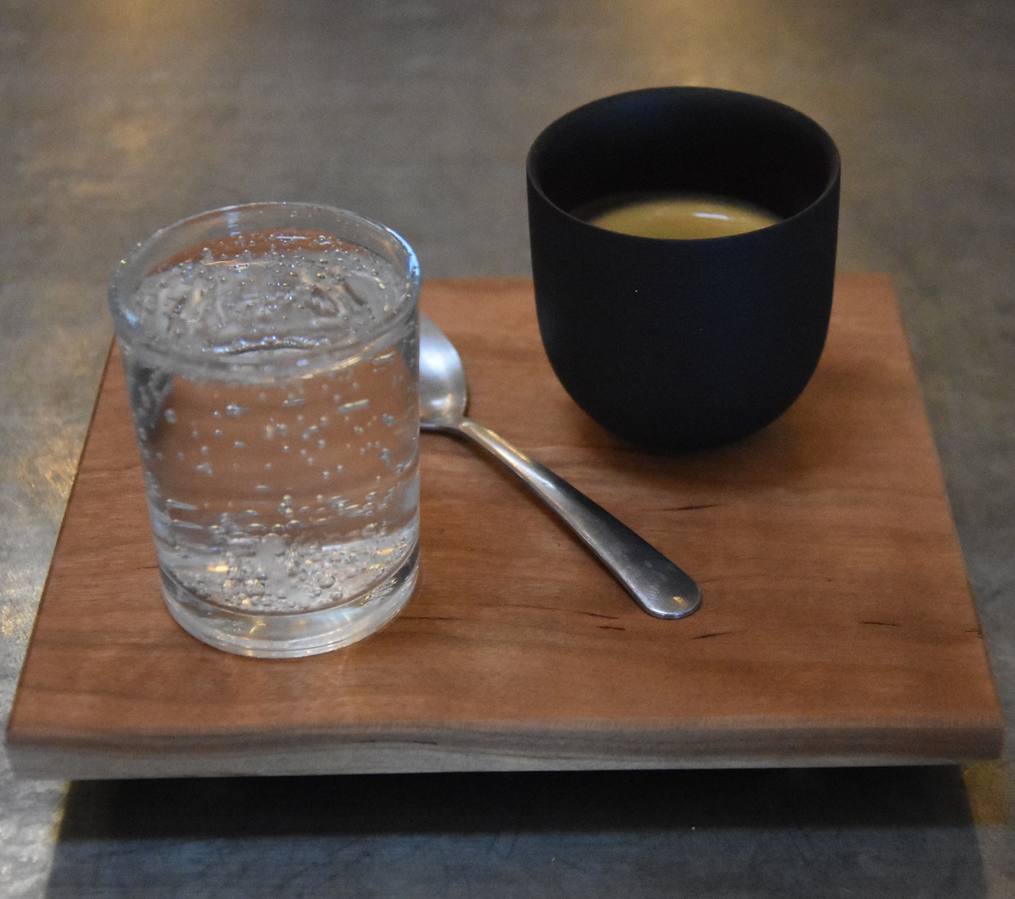 My espresso, a Colombian Geisha, roasted and served at Pair Speciality Coffee & Tea in Mesa, and presented on a square, wooden tray with a glass of water on the side.