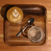 My cortado, made with the La Esperanza Colombian single-origin, roasted on-site and served in a glass, on a wooden tray, with a glass of water at the side.
