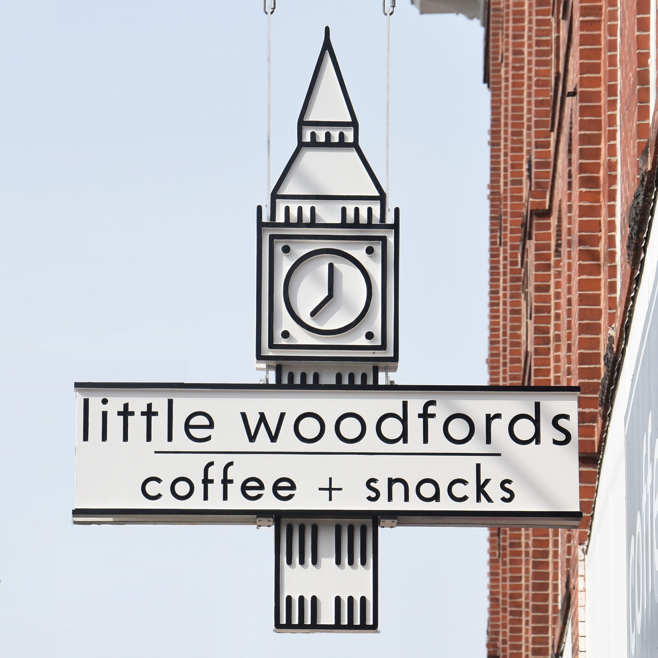 The Little Woodfords sign, hanging outside the store on Forest Avenue in Portland, Maine. It's a design based on the clock tower which sits atop of the building and reads "little woodfords | coffee + snacks".