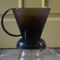 A Clever Dripper, sitting on top of a glass carafe, the brewed coffee draining through the bottom of the filter.