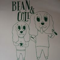 The new logo from the wall of Bean & Cole, featuring a pair of cartoon dogs, one holding an espresso cup and the other with a portafilter.