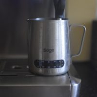My temperature-sensitive milk steaming jug, sitting under the steam wand of my Sage Barista Express home espresso machine.