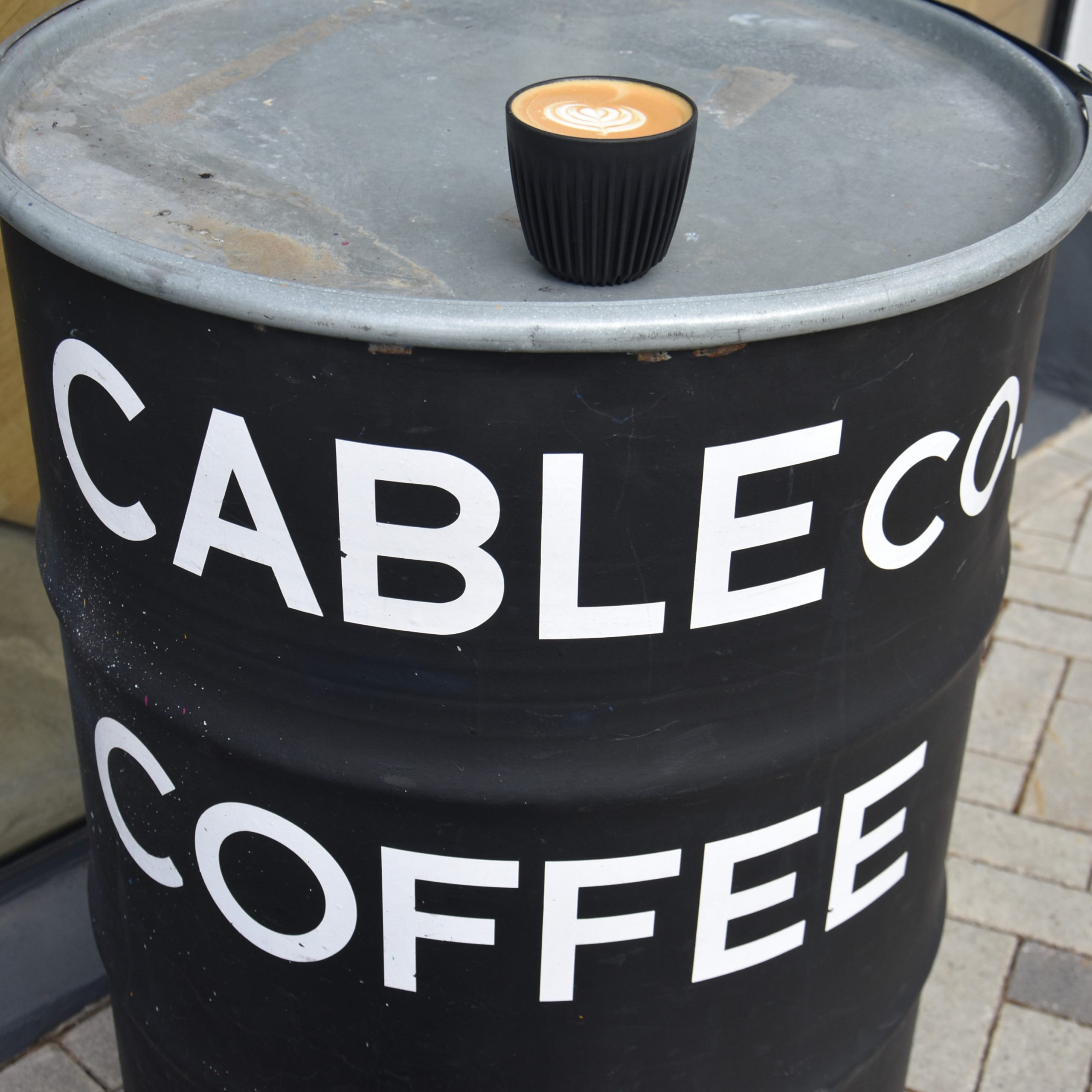 My decaf flat white on my HuskeeCup, sitting on an old barrel outside Cable Co. in The Aircraft Factory.