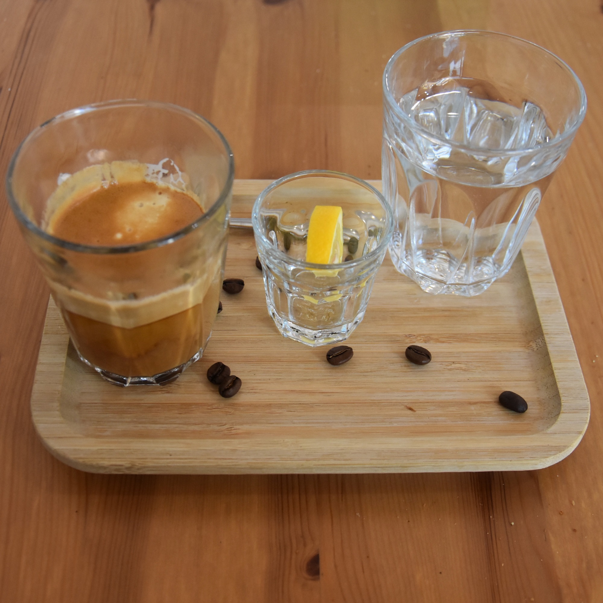 A commendably short cortado, served in a glass, and presented on a tray with a slice of orange and a glass of tap water.