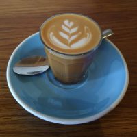 A beautiful cortado, served in a glass on a blue saucer, at The Penny Drop.
