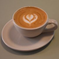 A flat white, served in a classic white cup but on an off-centre, non-circular saucer, at Coffee Circle Café – Mitte in Berlin.