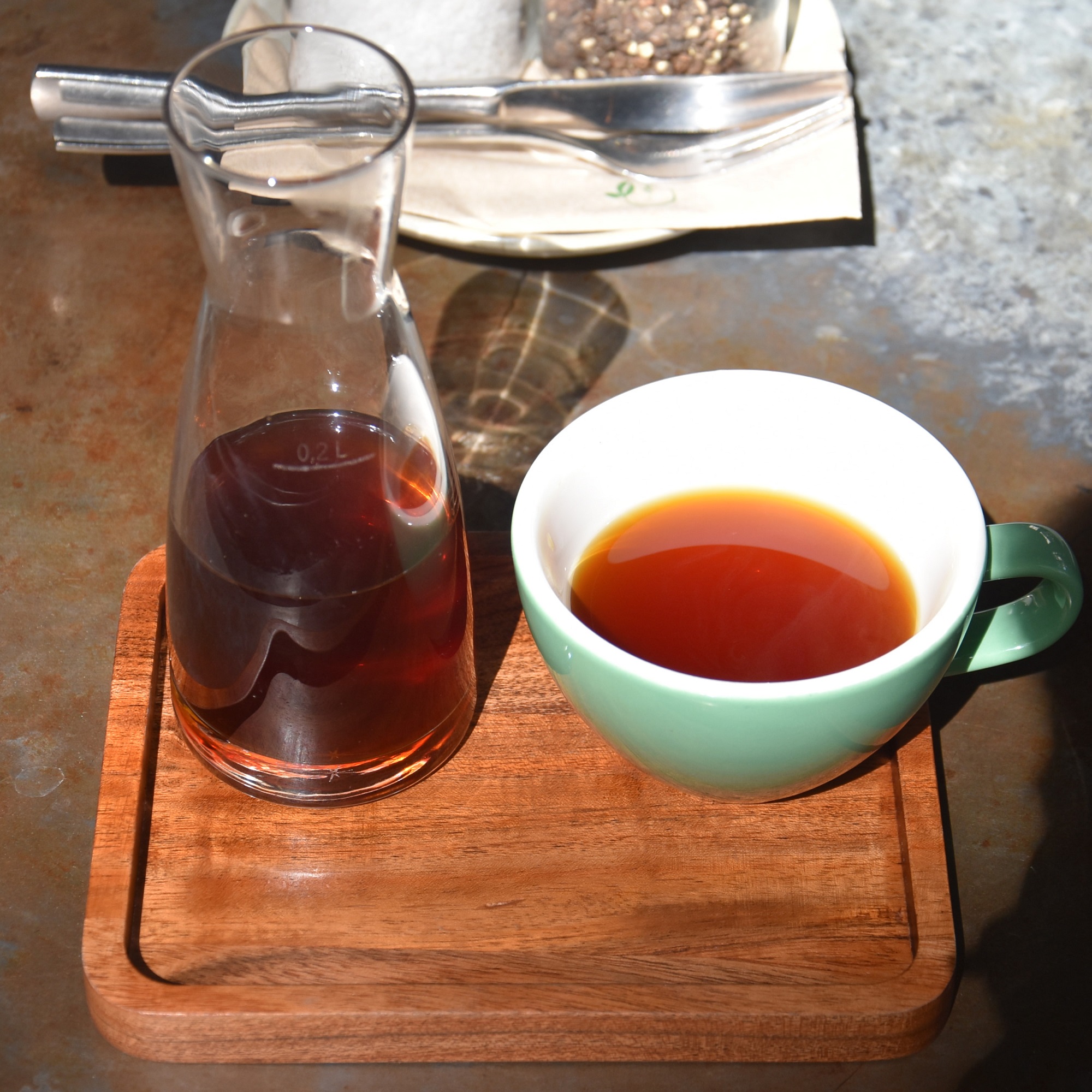 A beautiful carafe of a V60 of the Papua New Guinea (PNG) Grassroots, a fine, rich, fruity, full bodied naturally-processed coffee, roasted and served by KaffeeKirsche Café & Bakery on a wooden tray with a cup on the side.