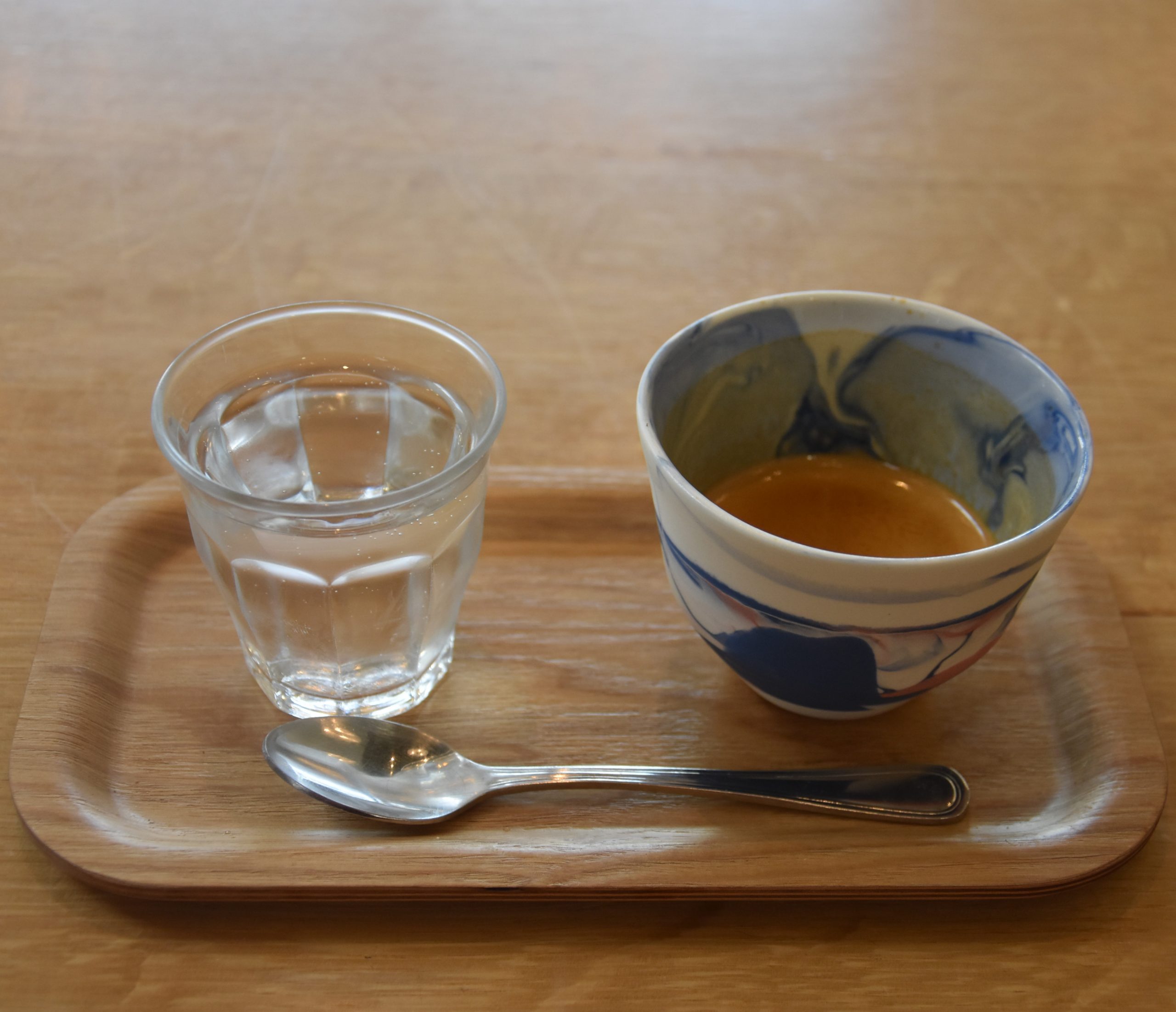 My espresso, the Baroida Estate, a naturally-processed coffee from Papua New Guinea, roasted and served by CoRo in its Coffee Room in Berkeley. The handleless ceramic cup is bespoke to CoRo, while the coffee is presented on a small, wooden tray with a glass of water on the side.