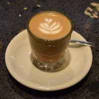 A lovely cortado, served in a glass on a large, white saucer, at Five Elephant, KaDeWe in Berlin.