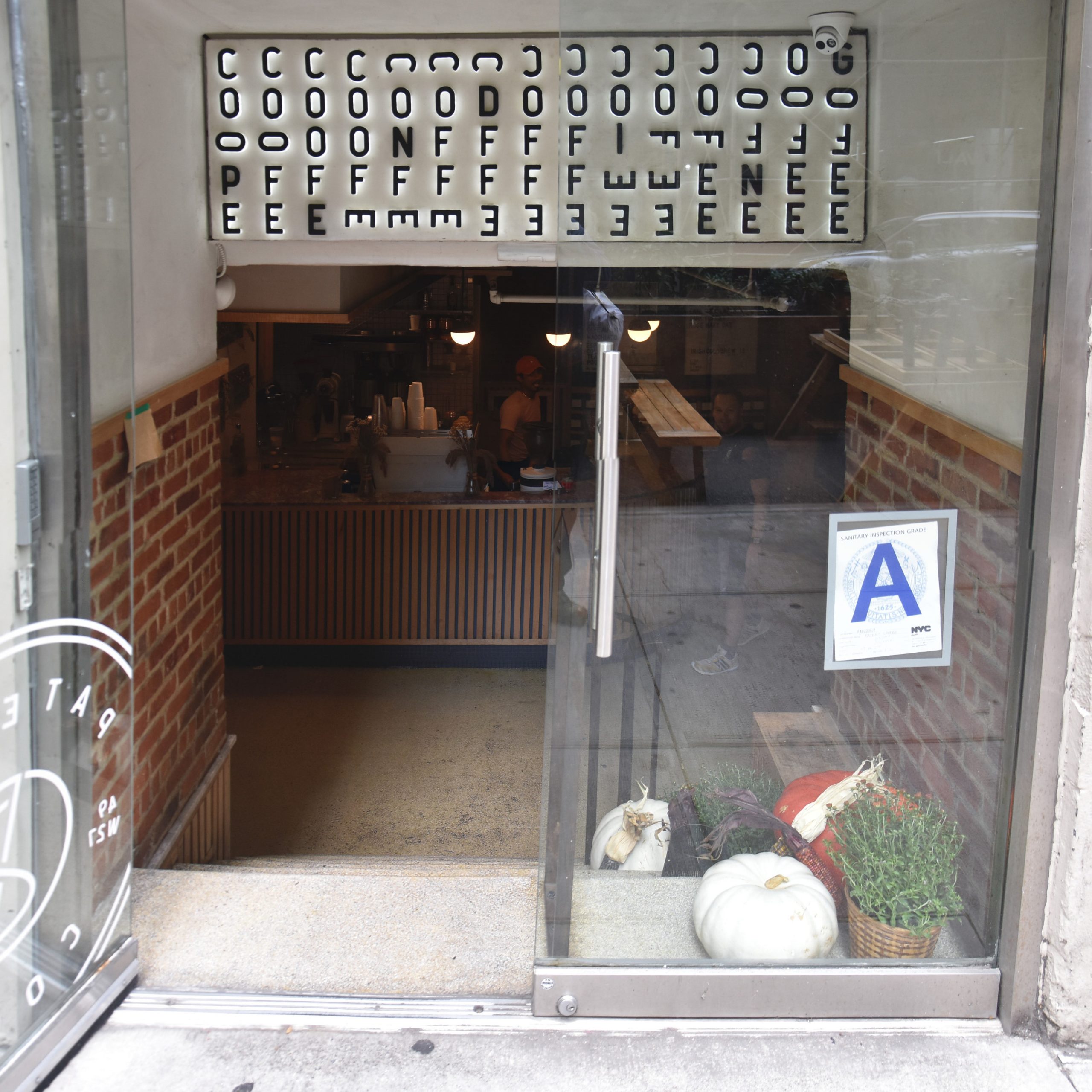 The glass double doors at the entrance to Patent Coffee in the Radio Wave Building in New York City. The left one is open, beoynd which are broad stone steps descending to basement, with the counter of Patent Coffee visible at the back.