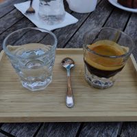 My espresso, served in a glass and presented on a wooden tray with a glass of water