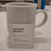 A mug of pour-over coffee made with the Gasharu Natural from Flip Coffee Roasters. An information card gives tasting notes of red cherry, dark grapes and demerara.