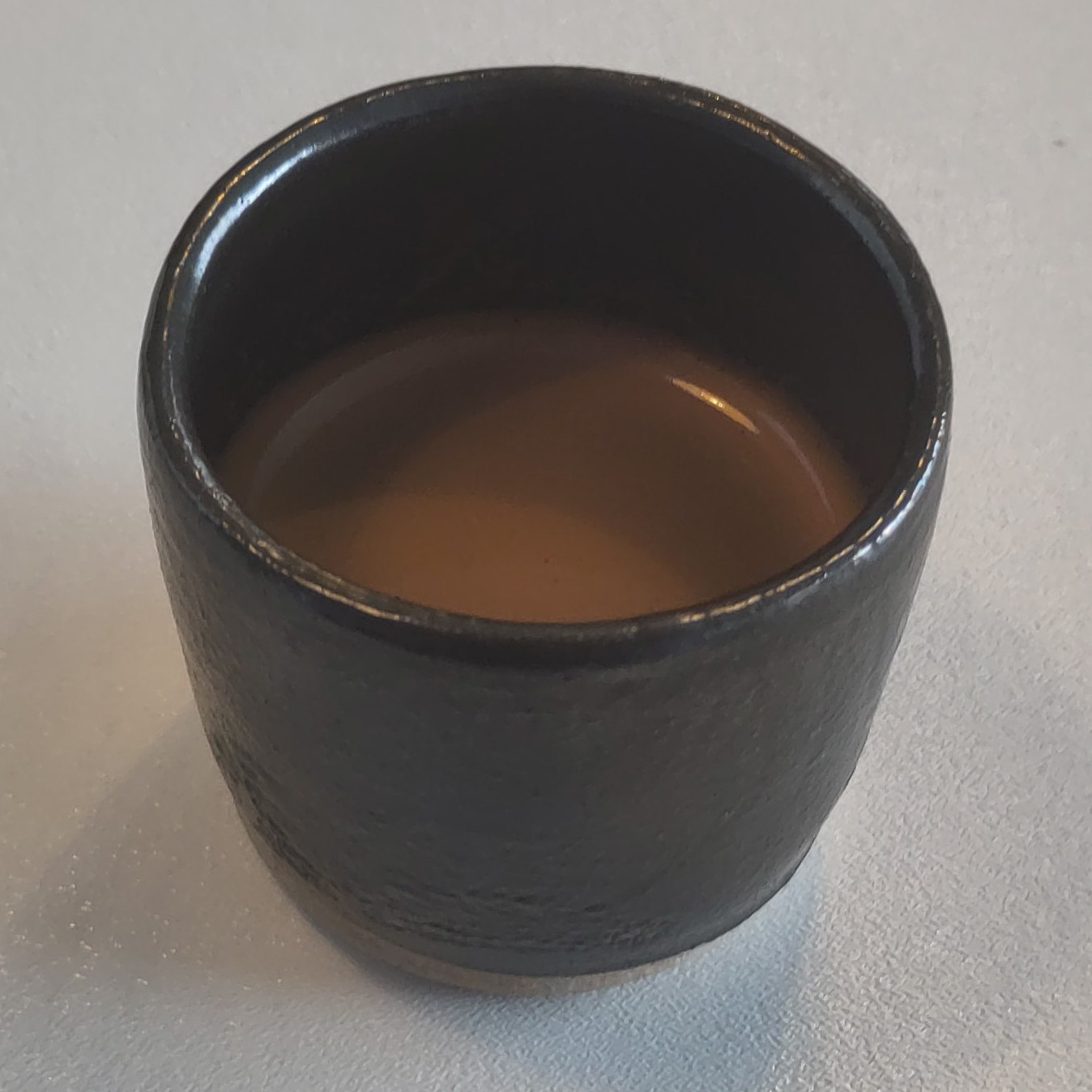 A lovely espresso in a dark, handleless ceramic cup