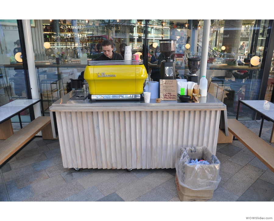 To the left of the door, there's this mobile counter with its bright yellow La Marzocco.