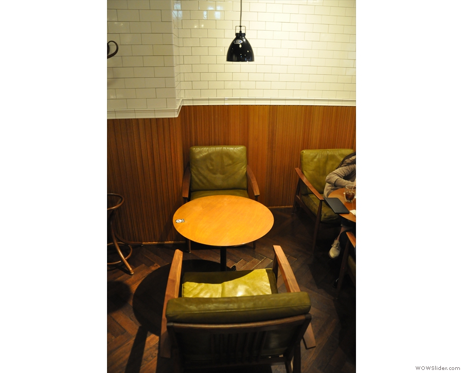 There are small, round tables with comfortable chairs up against the right-hand walll...