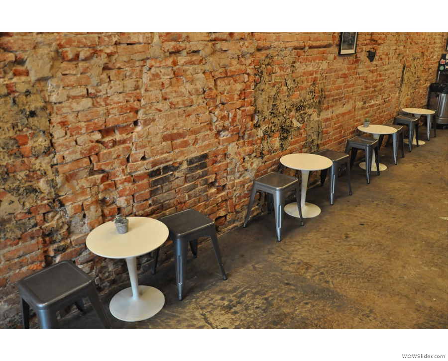 The seating is a row of two-person round tables against the bare-brick wall on the left.