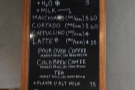 The concise coffee menu is on the wall to the right of the till...