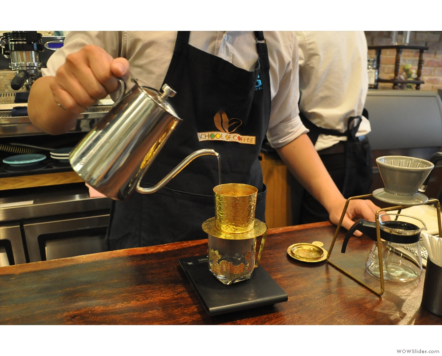 A steady, continuous pour, distributing the water evenly across the surface of the coffee.