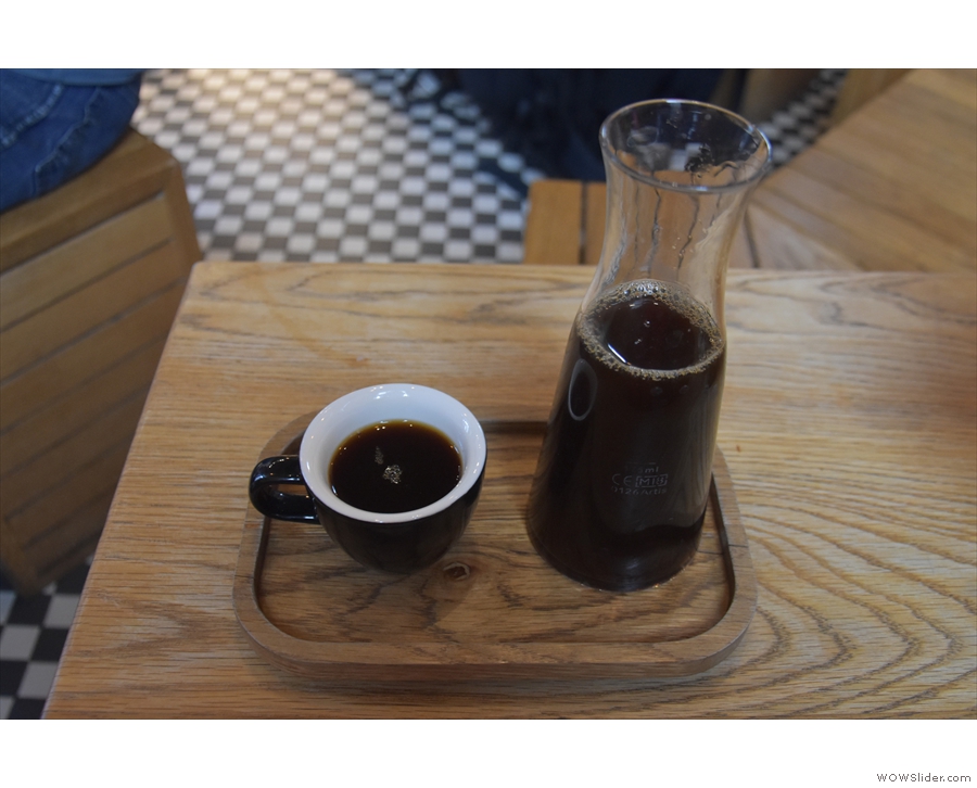 ... served in a carafe with a cup on the side, all presented on a wooden tray.