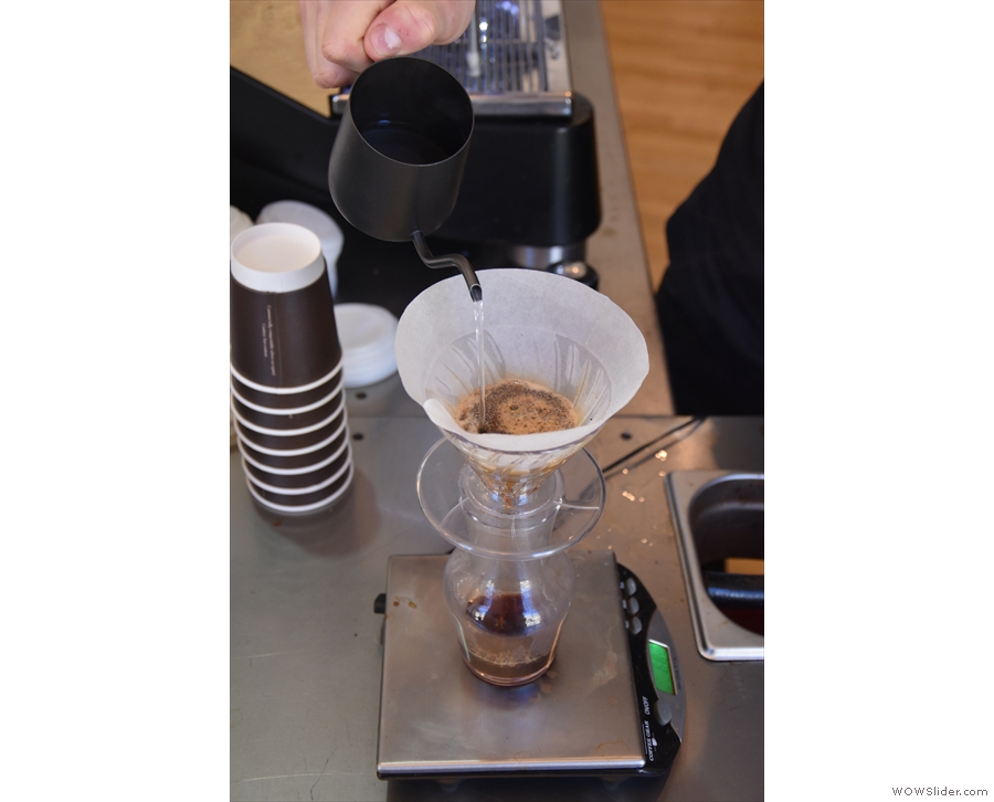 The pour is a controlled one, moving the spout across the surface of the coffee.