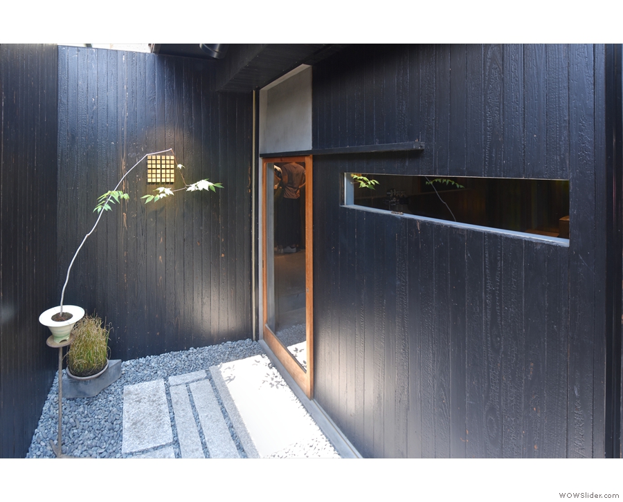A narrow, sheltered path leads down the side of the building, to a sliding glass door...